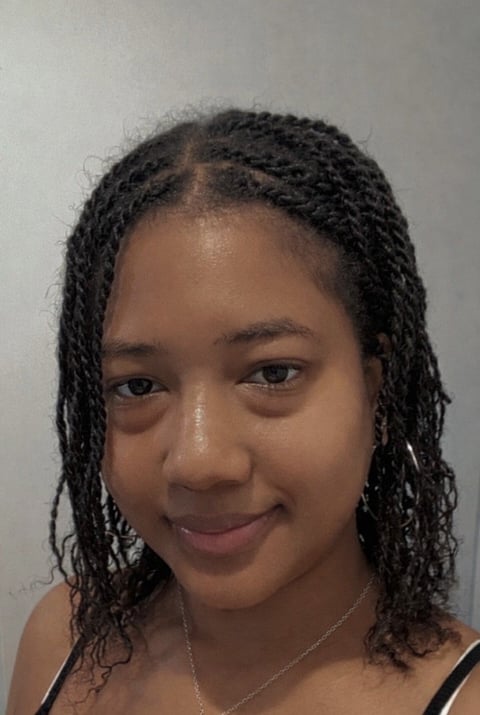 Portrait of a person with braided hair wearing a necklace against a light background