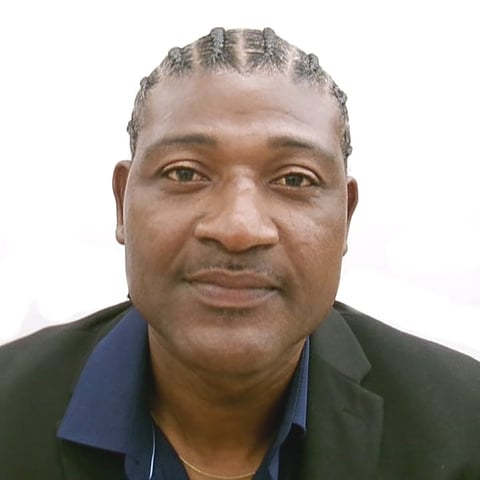Headshot of an older man with gray hair, wearing a dark green jacket over a blue shirt, against a white background